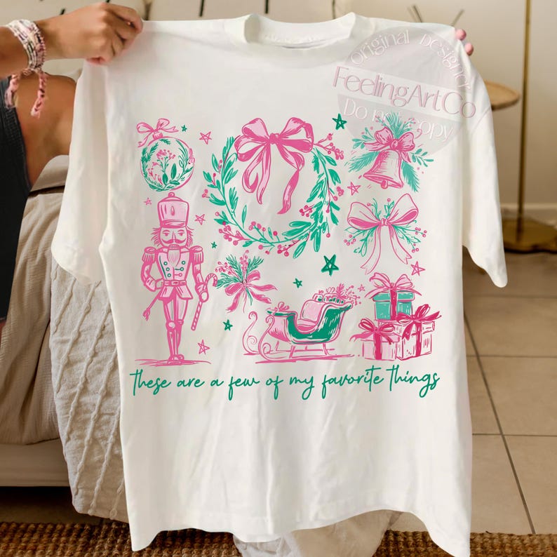 May include: White t-shirt with a festive design featuring pink bows, a wreath, a nutcracker, and a sleigh. The text "These are a few of my favorite things" is printed in green. The design includes stars and bell accents.