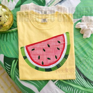 May include: Yellow t-shirt with a watermelon slice applique. The watermelon features a red and white gingham pattern, green rind, and black seeds. The shirt is part of a clothing collection.