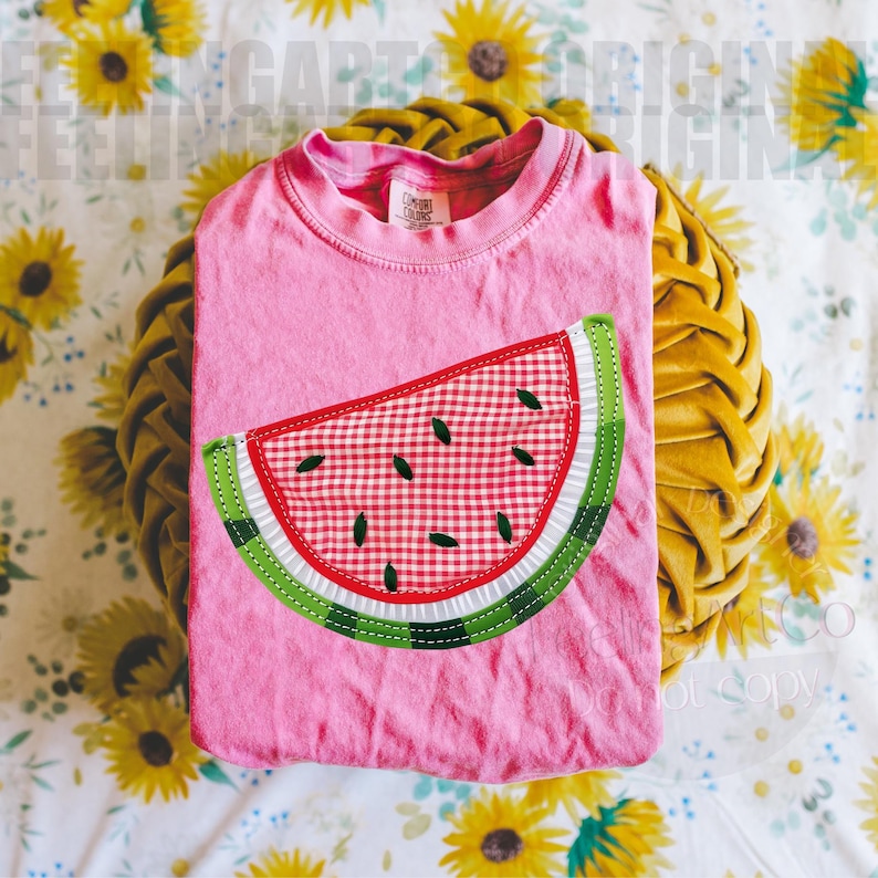 May include: A pink t-shirt with a watermelon slice applique. The watermelon design features a red and white checkered pattern, green rind, and black seeds. The shirt is folded on a yellow pillow with a floral background.