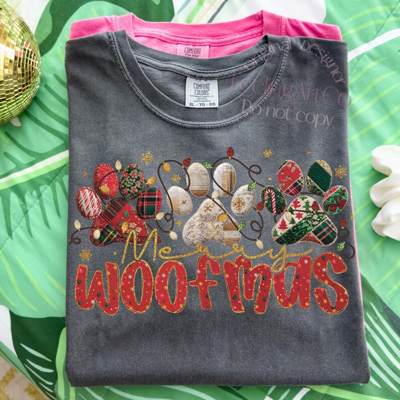 Puede incluir: Una camiseta gris Comfort Colors con un dise&ntilde;o festivo de huellas de patas y el texto "Merry Woofmas" en rojo y dorado. El dise&ntilde;o incluye luces navide&ntilde;as y huellas de patas decorativas. Una camiseta rosa es visible debajo.