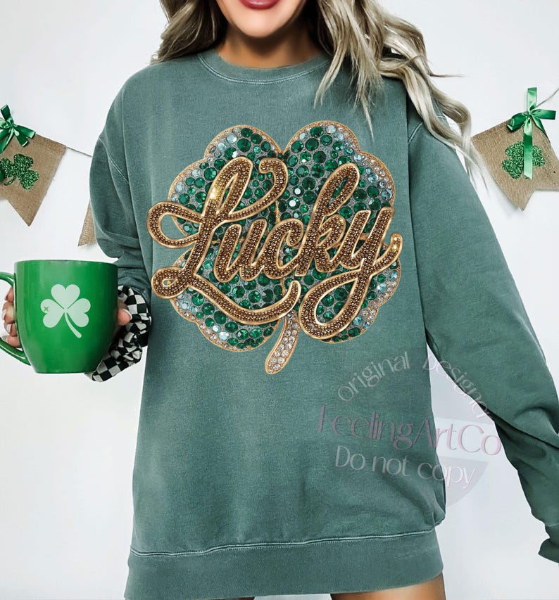 May include: Green sweatshirt with a large, sparkling shamrock design. The word "Lucky" is written in gold script across the shamrock. A green mug with a shamrock is held in the image. The sweatshirt has a relaxed fit.