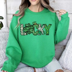 May include: A bright green sweatshirt with the word "LUCKY" in a playful design. The letter "L" is a leopard print, the "U" is a shamrock, and the "Y" has a horseshoe design. The sweatshirt is a crew neck.