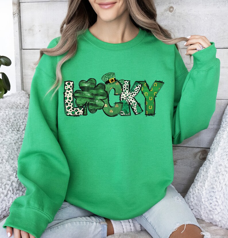 May include: A bright green sweatshirt with the word "LUCKY" in a playful design. The letter "L" is a leopard print, the "U" is a shamrock, and the "Y" has a horseshoe design. The sweatshirt is a crew neck.