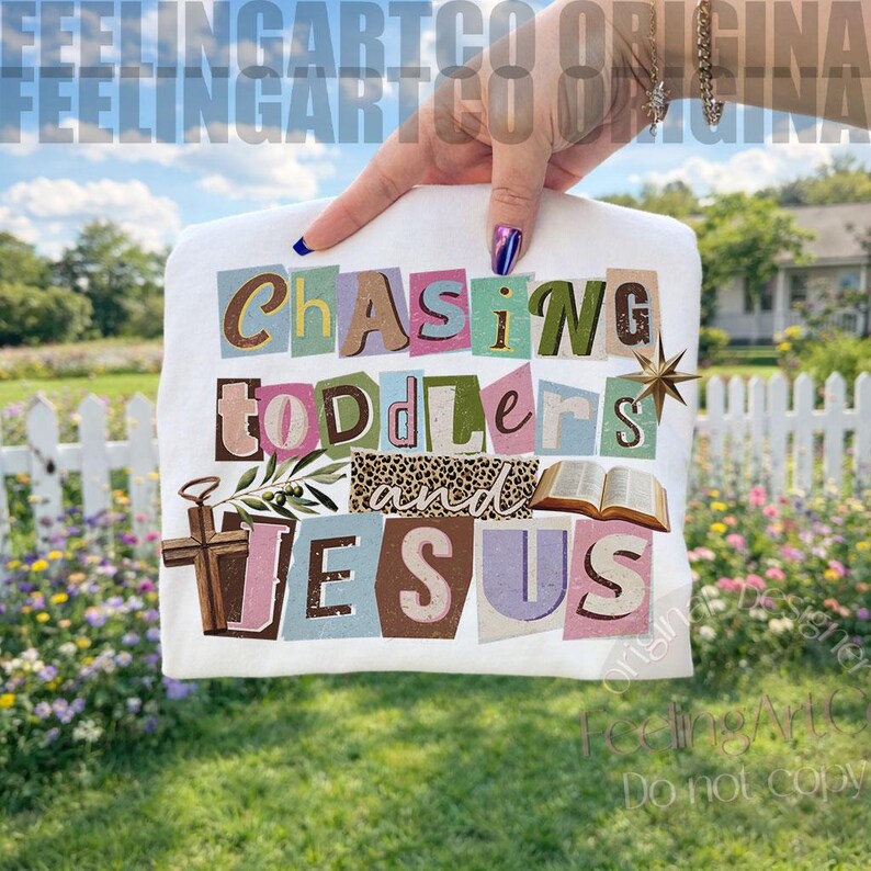 Pu&ograve; includere: T-shirt bianca con la scritta "Chasing Toddlers and Jesus" in uno stile colorato ritagliato. Il design include una croce, un libro aperto e una stella. La maglietta &egrave; tenuta su uno sfondo di erba verde e una staccionata bianca.