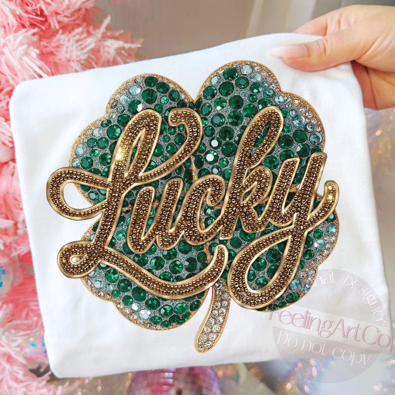 May include: White t-shirt featuring a large, embellished shamrock design. The shamrock is filled with green and clear rhinestones, with the word "Lucky" in gold, rhinestone-studded lettering. The design is centered on the shirt.