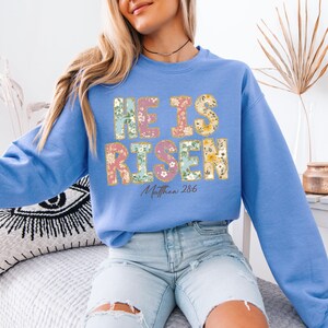 May include: A light blue sweatshirt with a floral design that says "He is Risen" and "Matthew 28:6".
