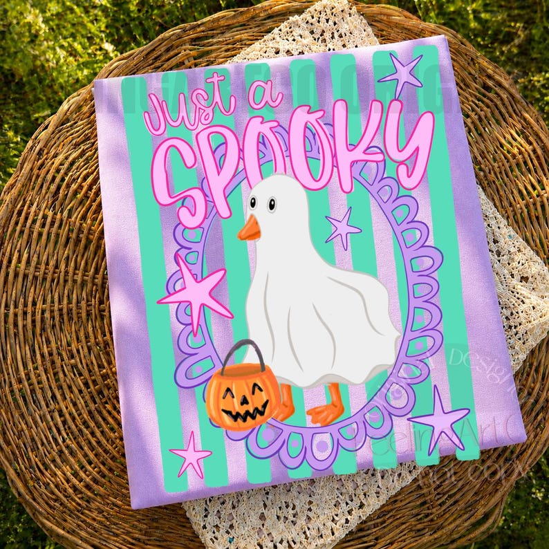 May include: A rectangular fabric print featuring a white ghost-costumed duck holding an orange jack-o'-lantern bucket. The design includes a purple scalloped oval frame, teal vertical stripes, pink stars, and the text Just a SPOOKY.