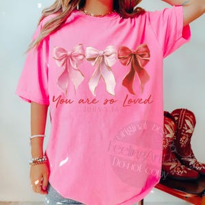 Pu&ograve; includere: T-shirt rosa acceso con tre fiocchi ad acquerello e bordi dorati. Il testo "You are so Loved" e "John 3:16" &egrave; stampato sotto. La maglietta ha una vestibilit&agrave; ampia e rilassata, perfetta per un look casual.