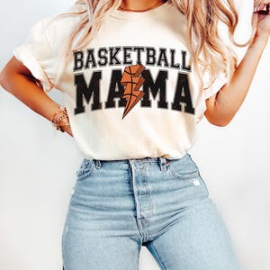 May include: A white t-shirt with the text "Basketball Mama" in black with a lightning bolt and basketball graphic.