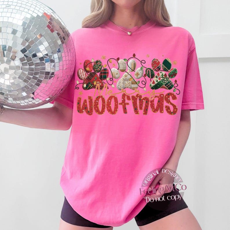 Puede incluir: Una camiseta rosa brillante con la palabra "WOOFMAS" en letras rojas. El dise&ntilde;o incluye huellas de patas decoradas con luces navide&ntilde;as y patrones de cuadros escoceses. La camiseta tiene un ajuste holgado y c&oacute;modo.