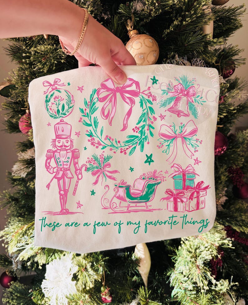 May include: A white tote bag featuring a Christmas-themed design in pink and teal. The design includes a wreath, bows, a bell, a nutcracker, a sleigh, and gifts. The text "These are a few of my favorite things" is printed at the bottom.