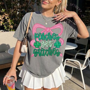 May include: Gray t-shirt with a pink bow and the text "Pinches get stitches" in green. The shirt also features green shamrocks. The model is wearing a white pleated skirt and carrying a small purse.