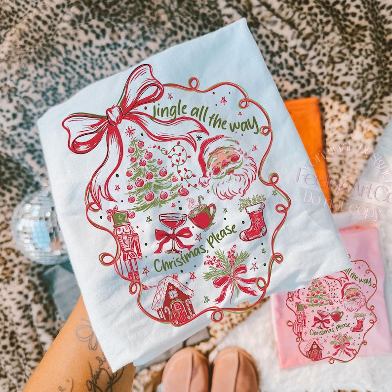 May include: A light blue t-shirt with a red and green Christmas design. The design includes a Christmas tree, Santa Claus, and the text "Jingle all the way" and "Christmas, Please".