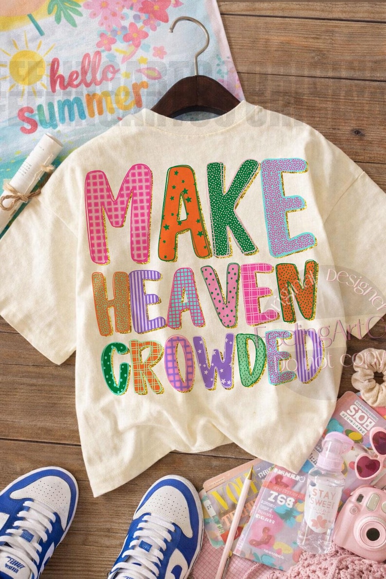 K&ouml;nnte beinhalten: Cremefarbenes T-Shirt mit dem Schriftzug "MAKE HEAVEN CROWDED" in bunten, gemusterten Buchstaben. Das Shirt h&auml;ngt an einem Holzb&uuml;gel. Weitere Artikel sind blau-wei&szlig;e Turnschuhe, Sonnenbrillen und eine Kamera.