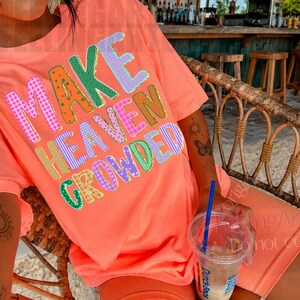 K&ouml;nnte beinhalten: Korallfarbenes T-Shirt und Shorts-Set mit dem Schriftzug "MAKE HEAVEN CROWDED" in bunten, gemusterten Buchstaben. Die Person sitzt in einem Korbstuhl und h&auml;lt ein Getr&auml;nk mit einem blauen Strohhalm.