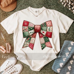 May include: A white t-shirt featuring a large, colorful bow design. The bow is composed of patchwork squares in red, green, and pink, with festive patterns. The text "Feeling ArtCo" and "digital download" are visible on the shirt.