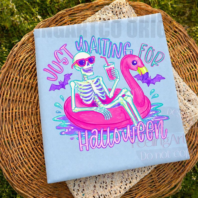 Peut inclure: T-shirt bleu clair avec un squelette portant des lunettes de soleil flottant sur un bou&eacute;e gonflable flamant rose. Le texte dit "Just Waiting for Halloween" avec des chauves-souris violettes et des d&eacute;tails d'eau.