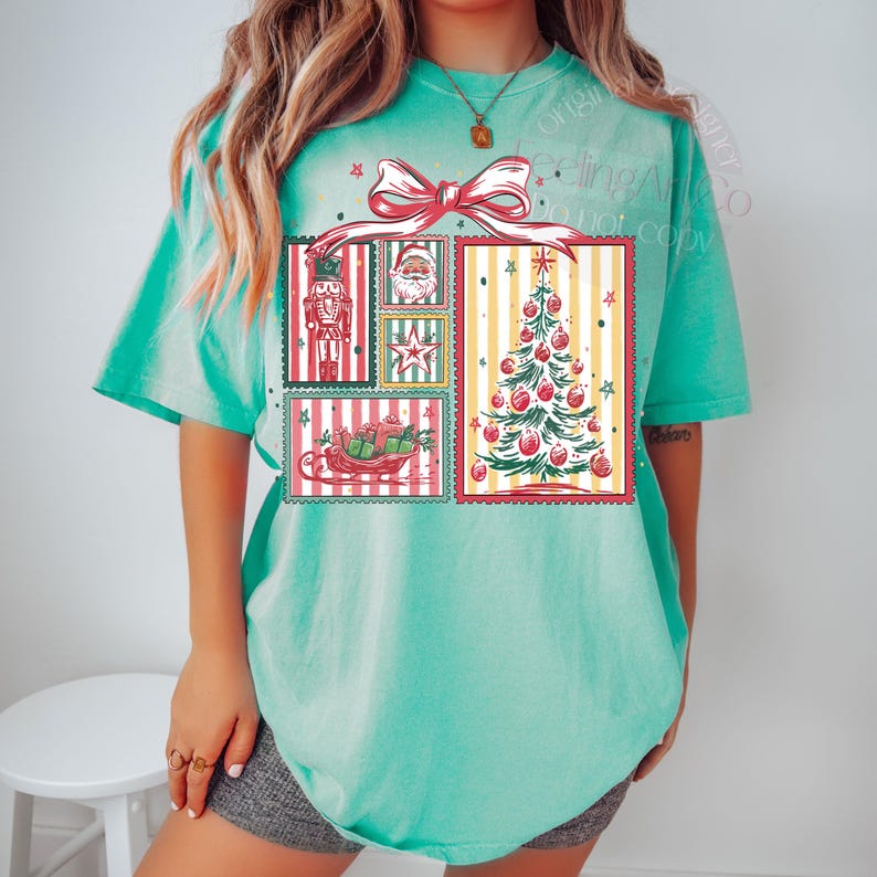May include: A turquoise short-sleeve t-shirt featuring a Christmas-themed graphic. The graphic includes a red bow, a Christmas tree, Santa Claus, a nutcracker, and a sleigh filled with gifts, all in a vintage postage stamp style.