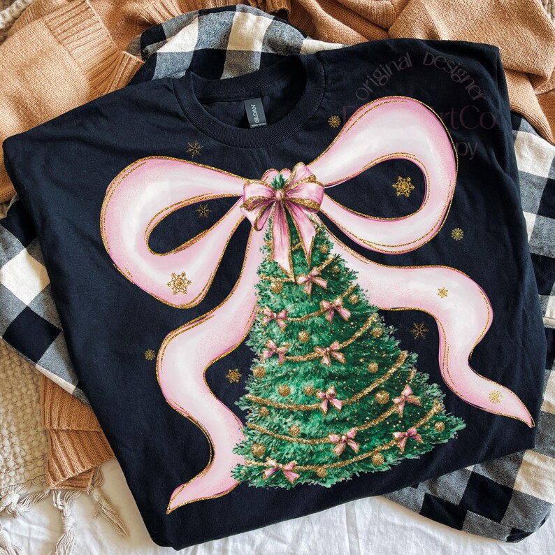 Pu&ograve; includere: T-shirt nera con un motivo a forma di albero di Natale. Il design include un grande fiocco rosa, un albero di Natale verde decorato con fiocchi rosa e ornamenti dorati e fiocchi di neve dorati. Il testo "Original Designer Art Co" &egrave; visibile.