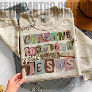 Pu&ograve; includere: Felpa color crema con la scritta "Chasing Toddlers and Jesus" in stile collage. Il design include una croce, un libro aperto e una stella. La felpa &egrave; abbinata a jeans blu e una collana floreale.