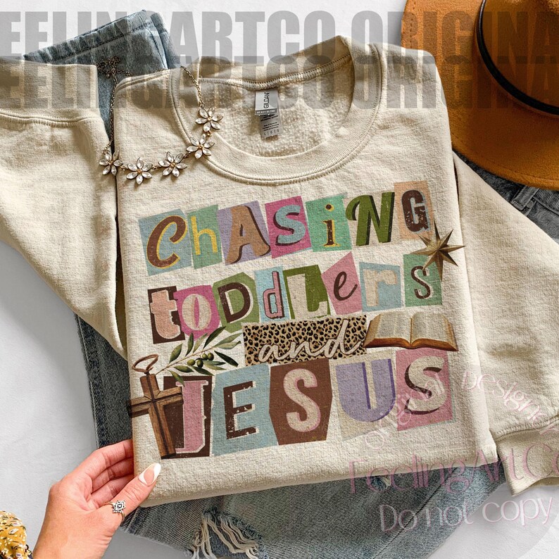 Pu&ograve; includere: Felpa color crema con la scritta "Chasing Toddlers and Jesus" in stile collage. Il design include una croce, un libro aperto e una stella. La felpa &egrave; abbinata a jeans blu e una collana floreale.