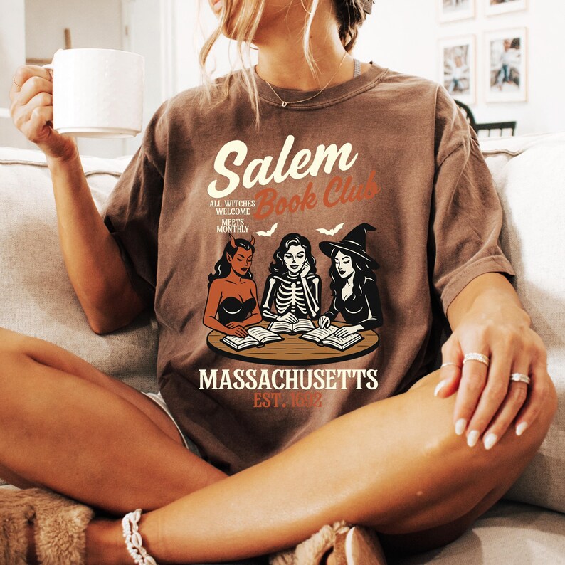 May include: Brown t-shirt with the text "Salem Book Club" and an illustration of three witches reading books. The shirt also includes the text "Massachusetts Est. 1692".