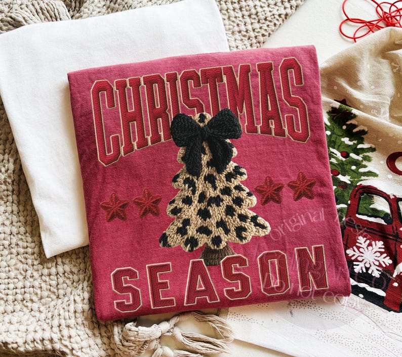 May include: A red Christmas-themed decorative pillow with the words "CHRISTMAS SEASON" in a collegiate font. The pillow features an embroidered leopard print Christmas tree with a black bow and red stars.