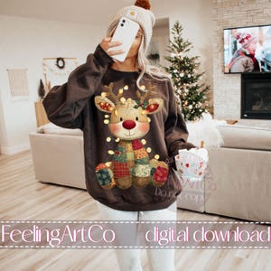 Puede incluir: Una sudadera marr&oacute;n con un dise&ntilde;o de reno navide&ntilde;o. El reno tiene una nariz roja, cuernos y luces de cadena. Lleva una bufanda de retazos y tiene una cara sonriente. El texto "FeelingArtCo digital download" est&aacute; en la parte inferior.