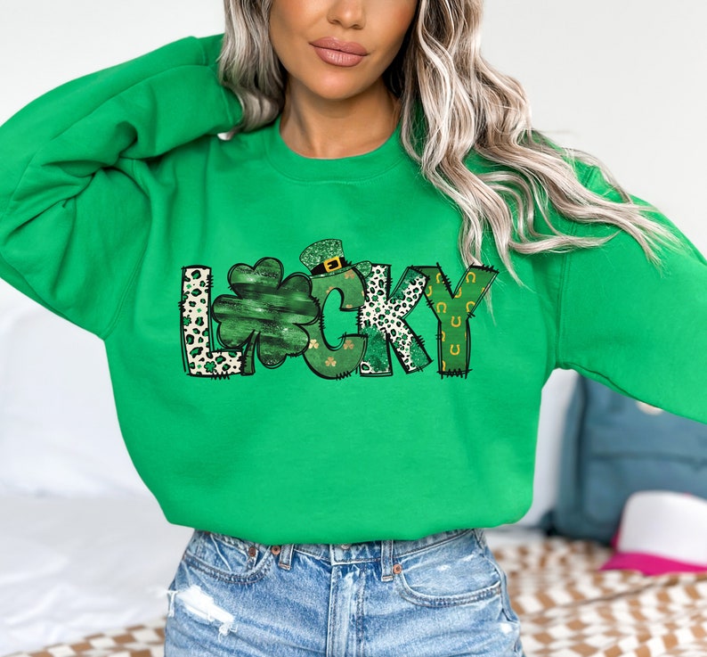 May include: A bright green sweatshirt with the word "LUCKY" in a whimsical design. The letter "L" has a leopard print pattern, the "U" is a shamrock, and the "Y" has a horseshoe design. The sweatshirt is perfect for St. Patrick's Day.