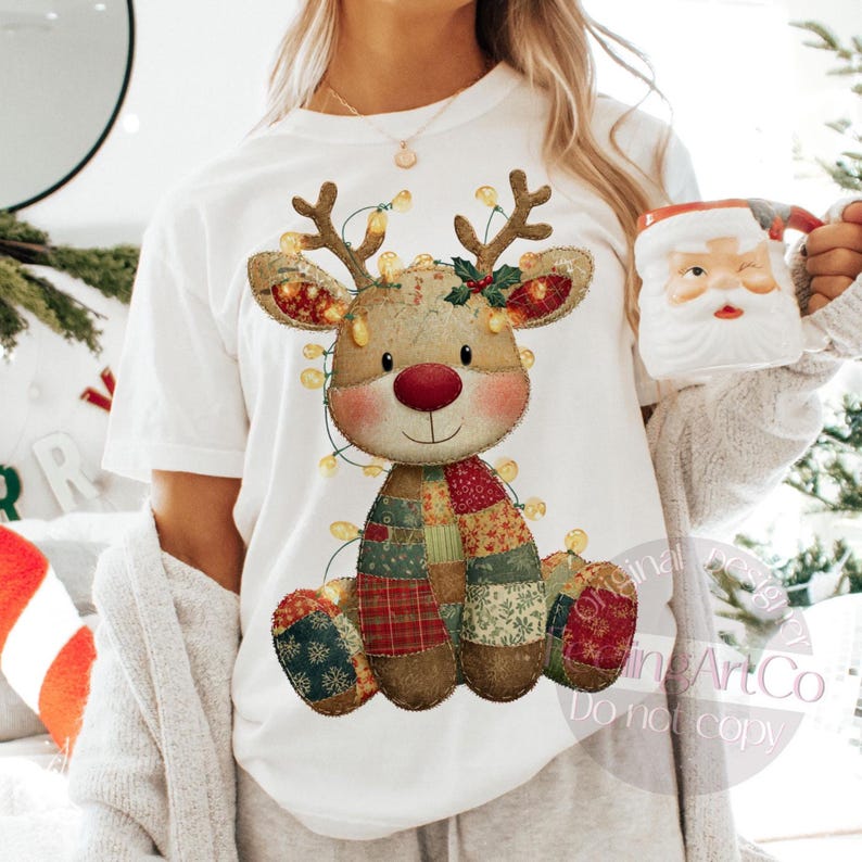 Puede incluir: Camiseta blanca con un dise&ntilde;o caprichoso de reno. El reno tiene un cuerpo de retazos, una nariz roja y est&aacute; adornado con luces de cadena. Una taza de Pap&aacute; Noel se sostiene en la mano. El dise&ntilde;o es festivo y adecuado para la temporada navide&ntilde;a.