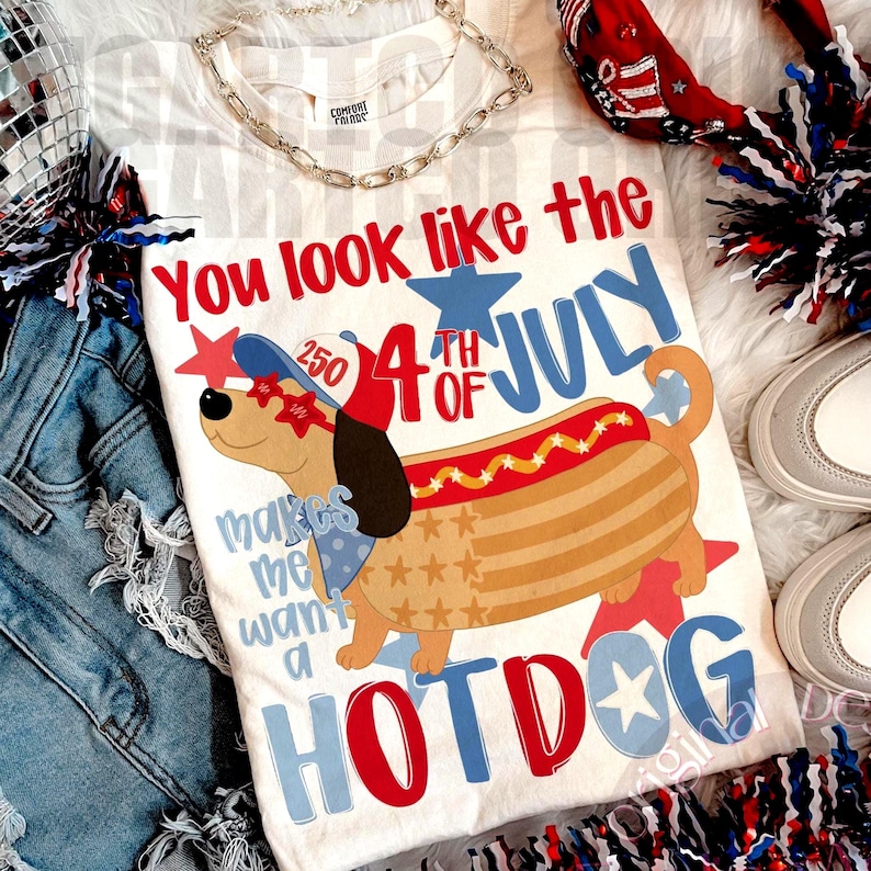 May include: A white t-shirt with a graphic of a dachshund dressed as a hot dog, with the text "You look like the 4th of July makes me want a HOTDOG". The shirt is decorated with red, white, and blue stars.