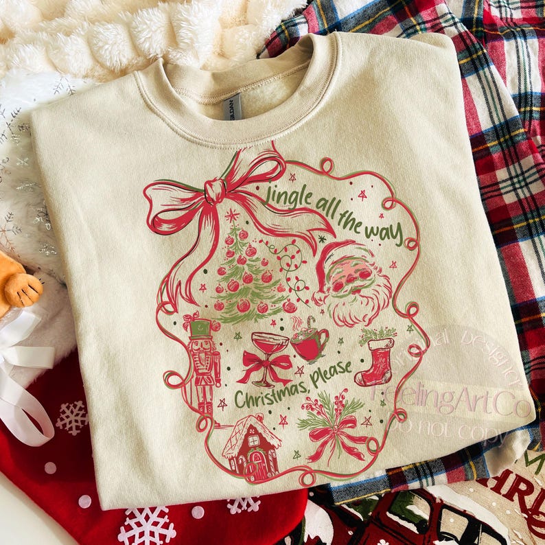 May include: Cream-colored sweatshirt with a festive Christmas design. The graphic includes a red bow, Christmas tree, Santa Claus, and the phrases "Jingle all the way" and "Christmas, please." The design is framed by a decorative border.