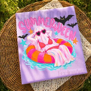 K&ouml;nnte beinhalten: Ein lila Leinwanddruck mit den Worten "Summerween" in Pink. Das Kunstwerk zeigt einen Geist mit herzf&ouml;rmiger Sonnenbrille und Bikini, der in einem rosa-orangenen Schwimmreifen schwimmt. Schwarze Flederm&auml;use und Sterne sind ebenfalls enthalten.