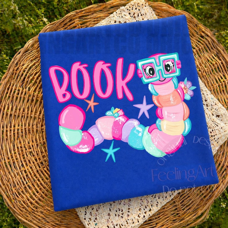 May include: A royal blue t-shirt featuring a colorful graphic of a segmented worm wearing teal-rimmed glasses. The word BOOK is printed in large pink letters above the worm, accompanied by small teal and orange star shapes and a flower.