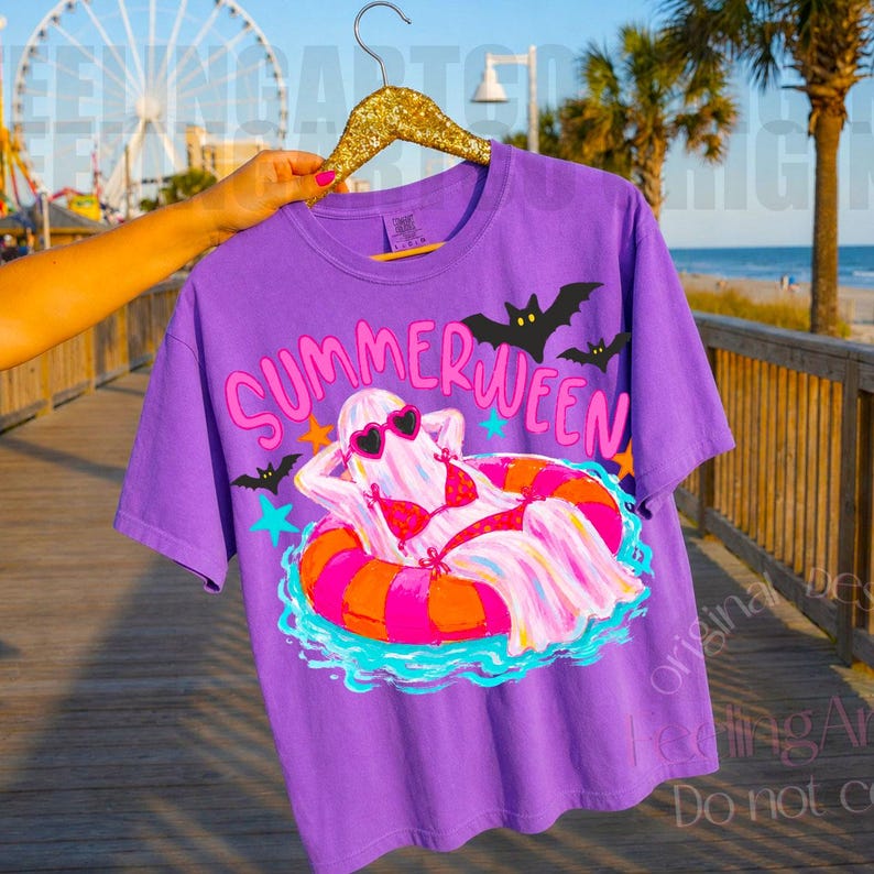 K&ouml;nnte beinhalten: Ein lila T-Shirt mit dem Schriftzug "SUMMERWEEN" in Pink und Gelb. Die Grafik zeigt ein Gespenst mit Sonnenbrille und Bikini, das auf einem bunten Schwimmring treibt. Schwarze Flederm&auml;use und blaue Sterne sind ebenfalls abgebildet.