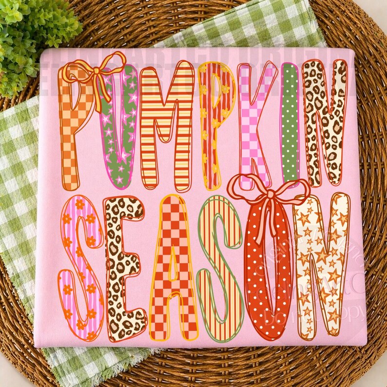 May include: A light pink fabric square featuring the text PUMPKIN SEASON in large, multi-patterned letters. The letters display various designs including orange and white checkers, green stars, leopard print, orange stripes, and polka dots.
