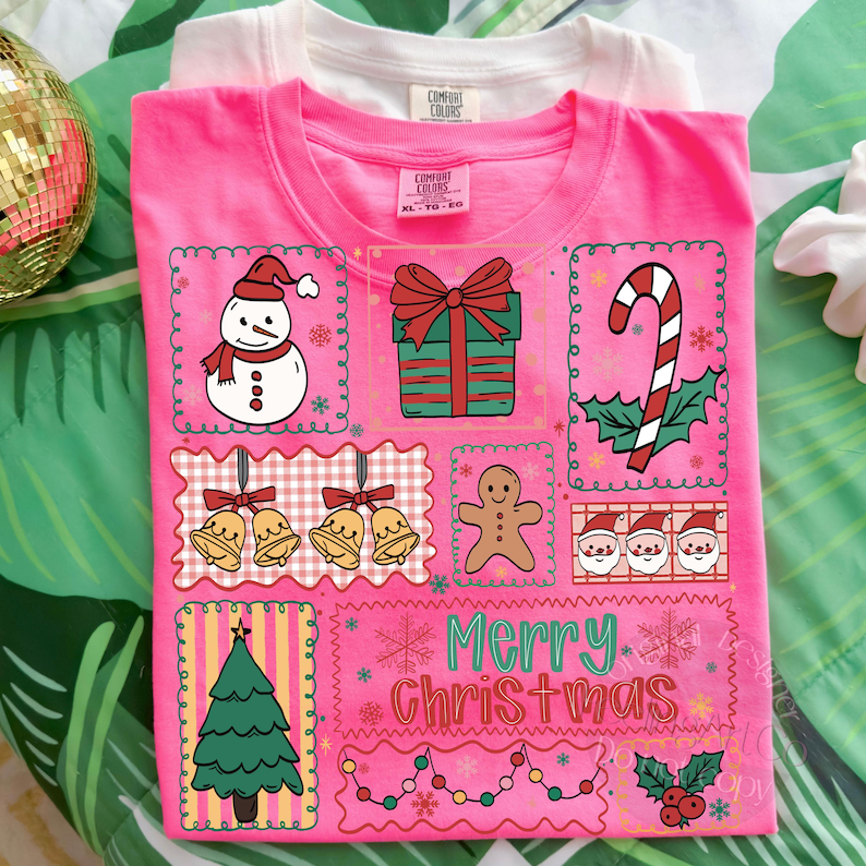 May include: A pink t-shirt with a festive Christmas design. The design includes a snowman, gift, candy cane, bells, gingerbread man, Santa faces, and a Christmas tree. The words "Merry Christmas" are also featured.