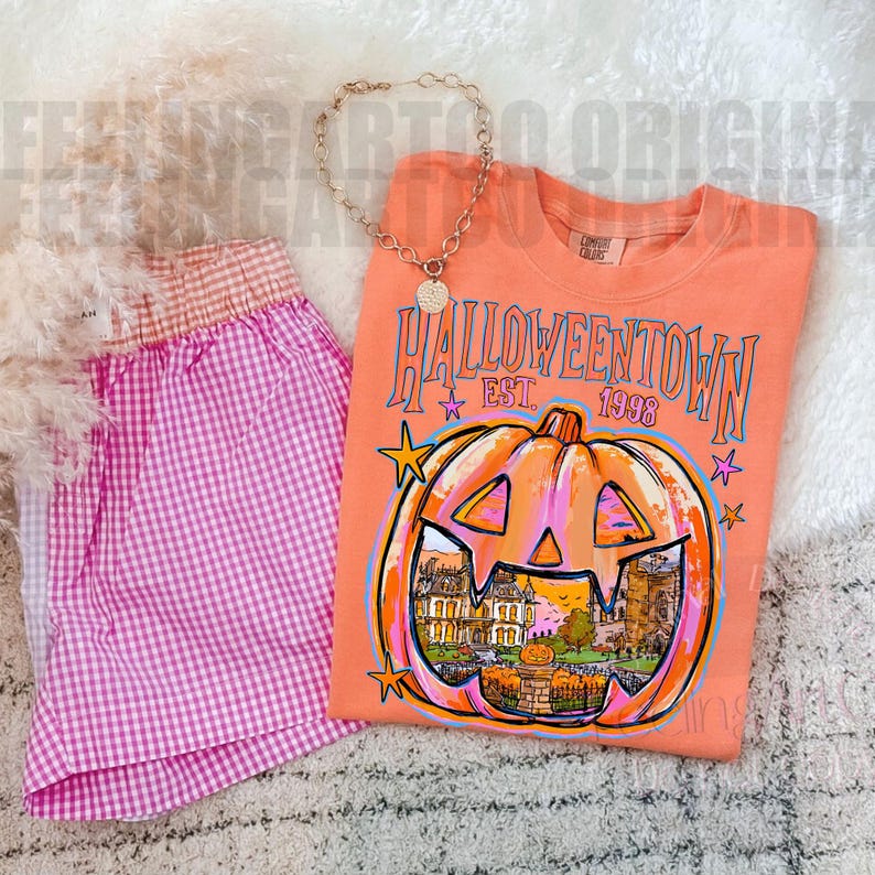 May include: An orange t-shirt featuring a graphic of a jack-o'-lantern with a house inside, the text HALLOWEENTOWN EST. 1998, and stars, paired with pink and white gingham shorts and a gold-toned chain necklace with a circular pendant.