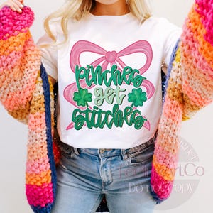 May include: White t-shirt with a pink bow and the text "Pinches get stitches" in green. The shirt is paired with light blue jeans and a colorful, chunky knit cardigan in shades of pink, orange, yellow, and blue.
