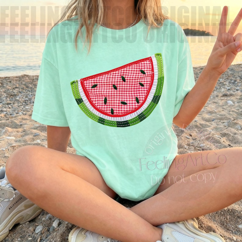 May include: A light green t-shirt featuring a watermelon slice design. The watermelon slice has a red and white checkered pattern, green rind, and black seeds. The shirt is a relaxed fit.