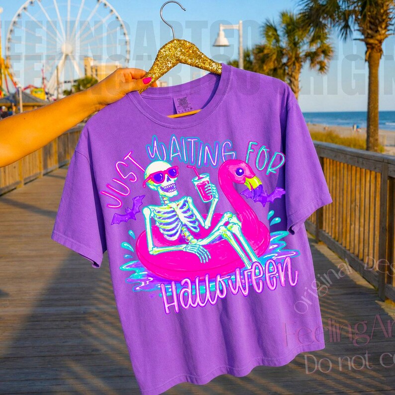Peut inclure: T-shirt violet avec un motif squelette portant des lunettes de soleil sur un bou&eacute;e flamant rose. Le texte "Just Waiting for Halloween" est imprim&eacute; en n&eacute;on. Le design comprend des chauves-souris.