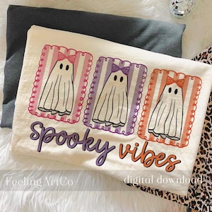 May include: Off-white t-shirt featuring three cartoon ghosts with bows in pink, purple, and orange frames. The shirt has the words "Spooky Vibes" in purple and orange. The shirt is a digital download.