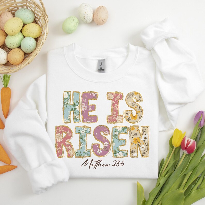 May include: White sweatshirt with a floral design that says "He is Risen" with the scripture reference "Matthew 28:6" underneath.