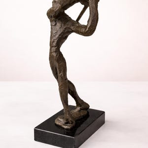 Puede incluir: Escultura de bronce de un golfista en pleno swing, montada sobre una base rectangular de m&aacute;rmol negro. La figura est&aacute; detallada con superficies texturizadas y posa con un palo de golf. Es un objeto decorativo.