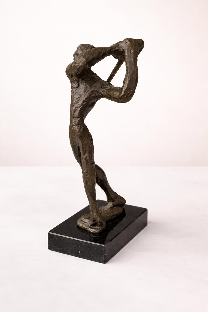 Puede incluir: Escultura de bronce de un golfista en pleno swing, montada sobre una base rectangular de m&aacute;rmol negro. La figura est&aacute; detallada con superficies texturizadas y posa con un palo de golf. Es un objeto decorativo.