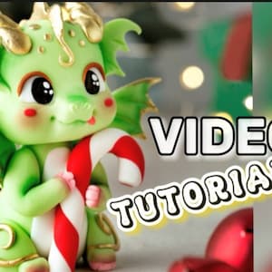 May include: A green sugar paste dragon figurine holding a candy cane. The dragon has large eyes and a cute expression. The text "VIDEO TUTORIAL" is in the background.
