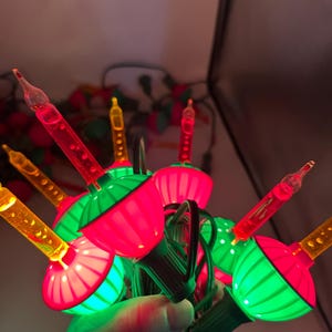 May include: A cluster of vintage Christmas lights. The bulbs are a combination of red, green, and yellow, with a classic teardrop shape. The lights are strung together with a green wire.