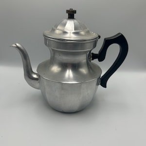 May include: A silver aluminum coffee pot with a black plastic handle. The pot has a lid with a small knob on top.