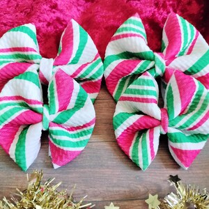May include: Four red and green striped fabric bows. The bows are made of a soft, textured fabric and are tied in a classic bow shape.