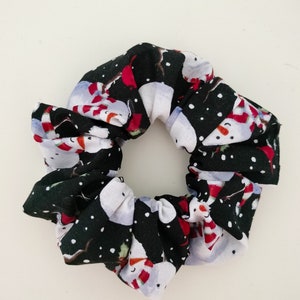 May include: A black and white scrunchie with a snowman pattern. The scrunchie is made of fabric and has a white background with black snowmen and red accents.